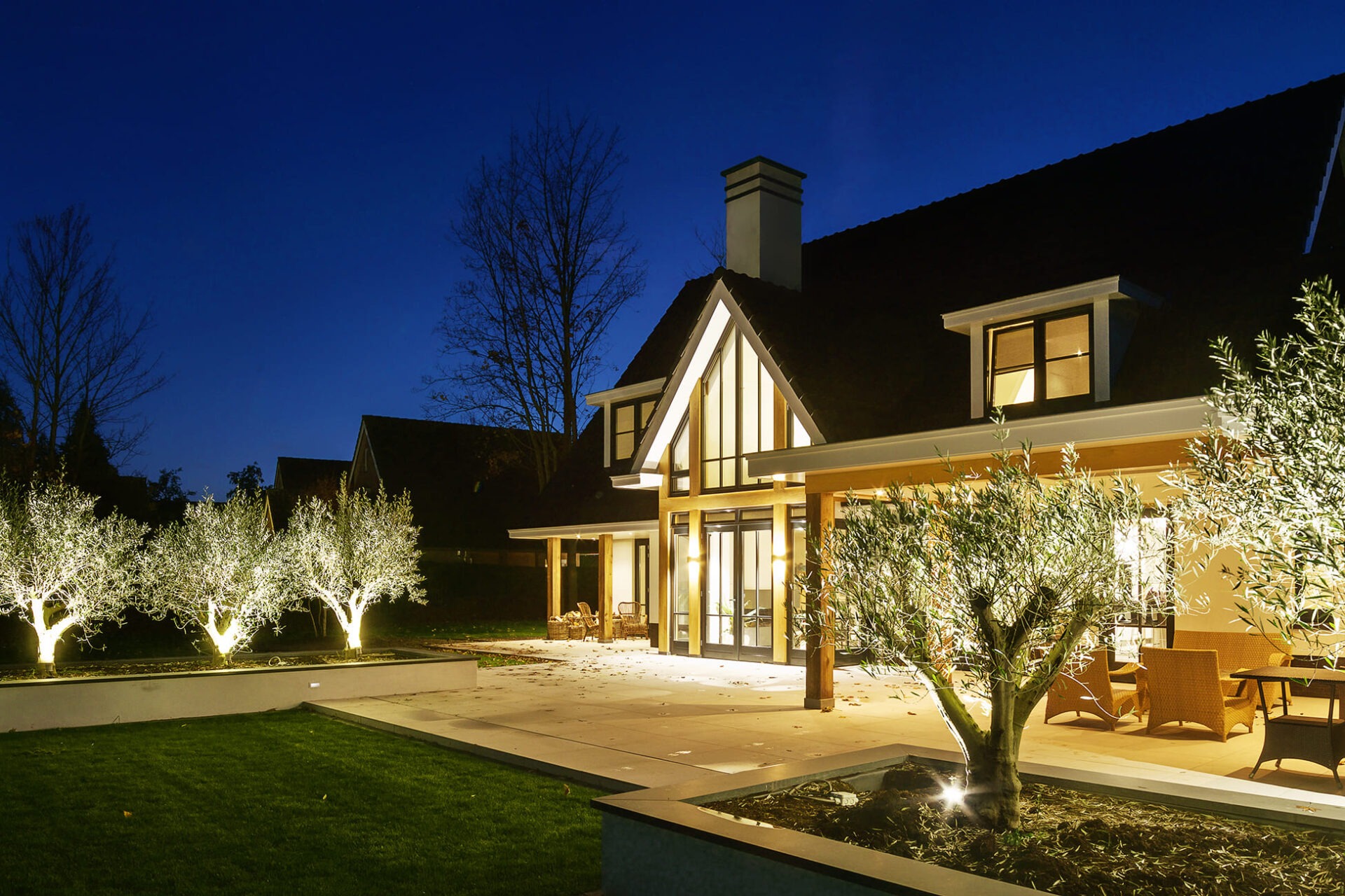 Achterzijde van Villa BB gezien vanuit de achtertuin. Het is avond waardoor je de verlichting goed ziet.