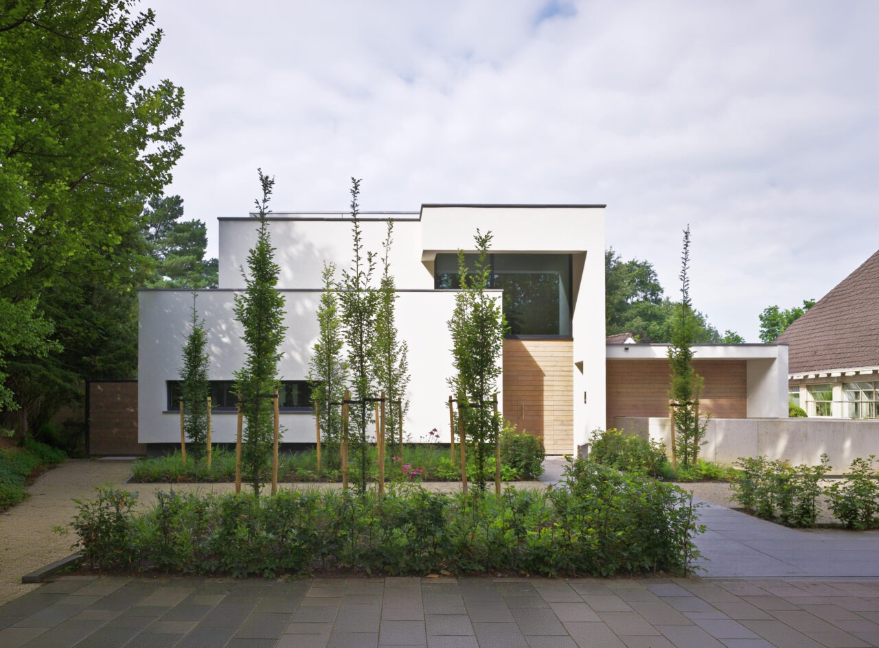 Vooraanzicht van villa bo. Het is een witte strakke moderne villa met een groene voortuin.