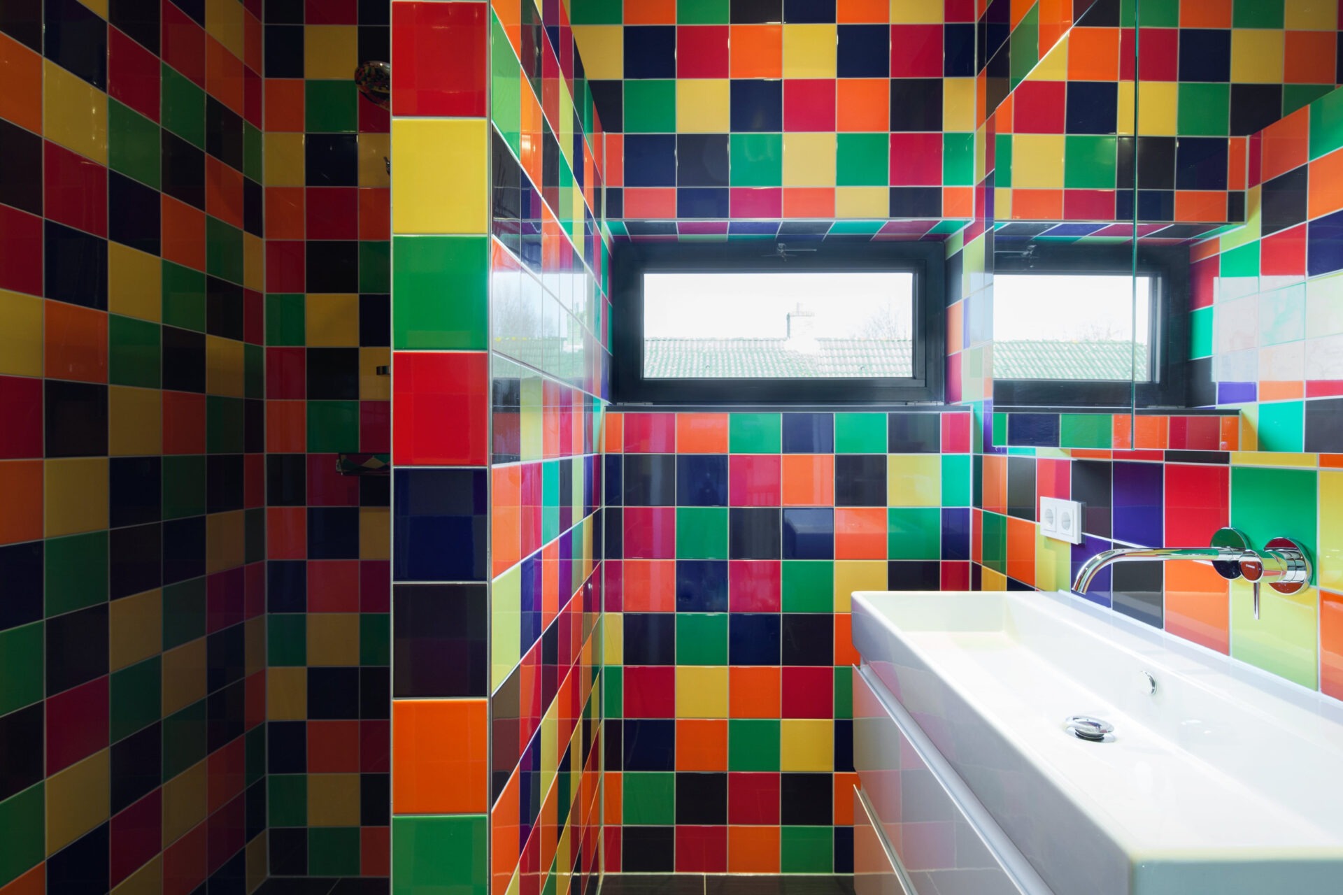 Badkamer met kleurrijke tegels. De tegels zijn rood, geel, groen, blauw, oranje en roze