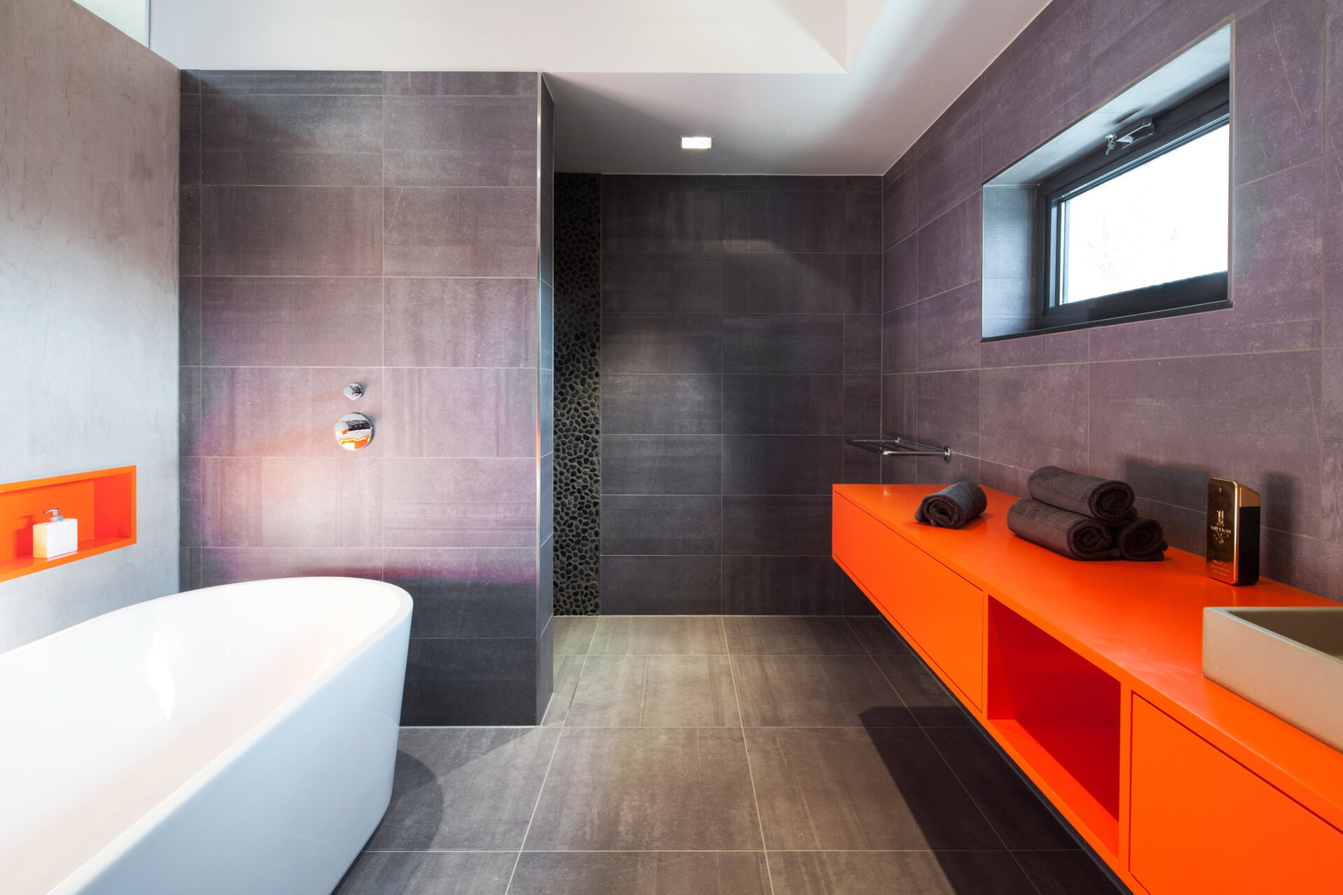 Badkamer met groot ligbad en een fel oranje badkamer meubel