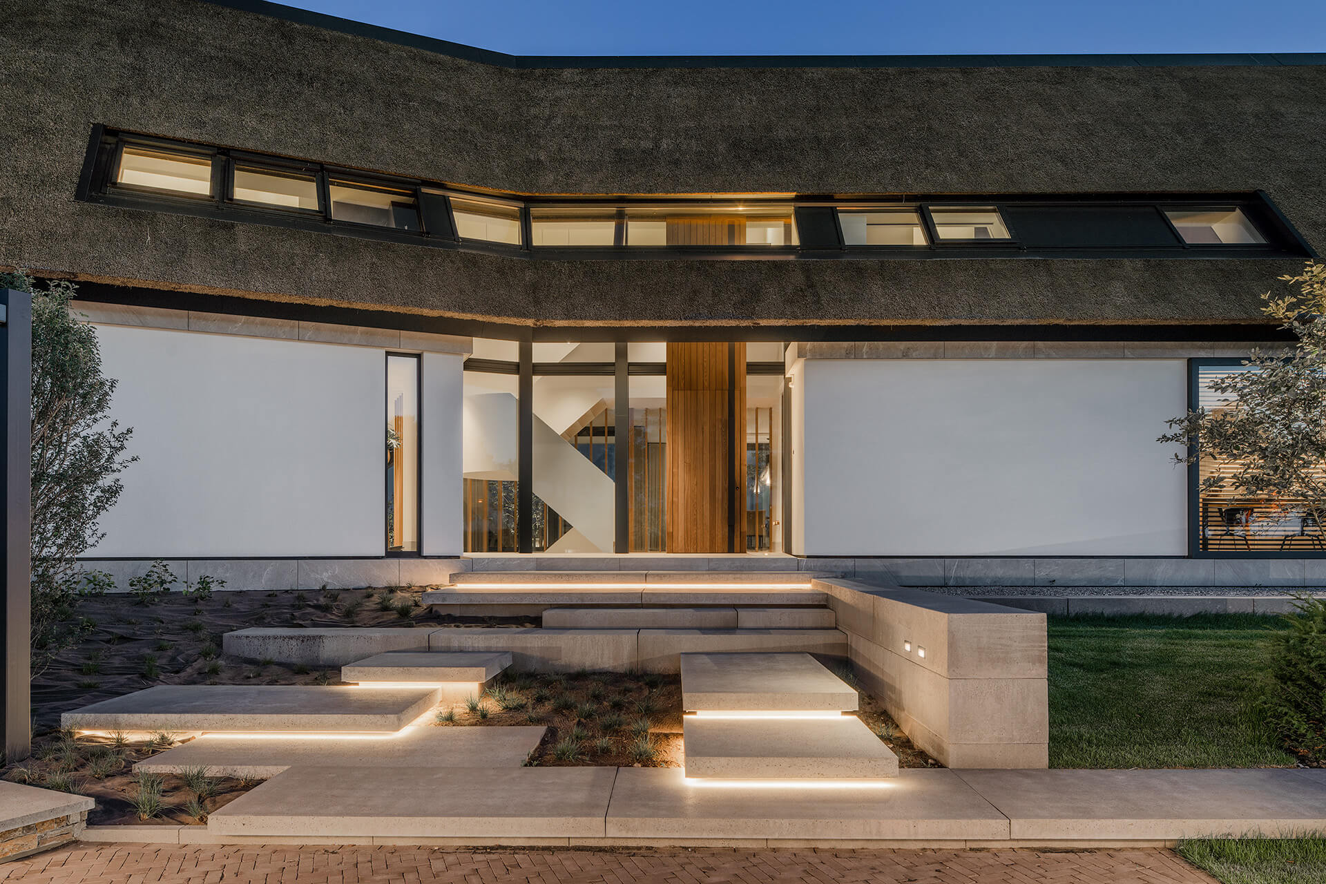 Detailfoto van de entree van Villa VS met een stenen trap verlicht met ledverlichting. Het is schemerig, waardoor je duidelijk de tuinverlichting ziet