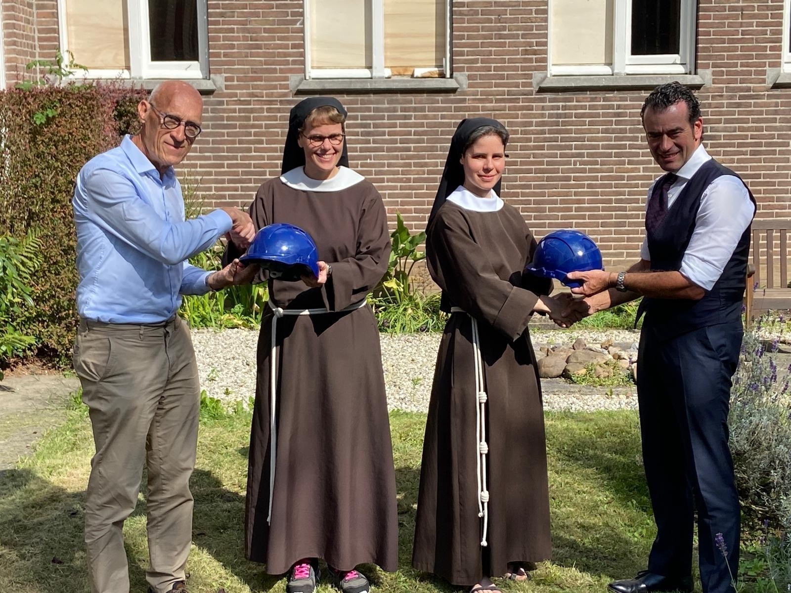 Bouwhelmen worden overhandigd door zusters aan wethouder Sidney van den Berg van de Gemeente Oss en frater Broer Huitema, bestuurslid van de Konferentie Nederlandse Religieuzen.