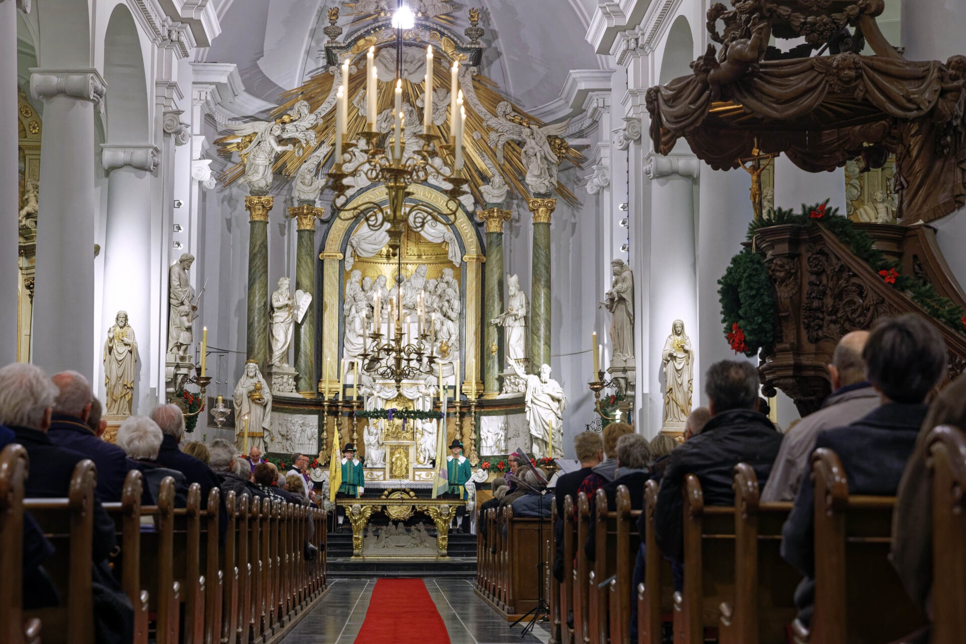 Binnenzijde van een volle Bartholomeuskerk. Op de voorzijde mensen in kerkbanken. Voor het altaar staan twee leden van het Gilde