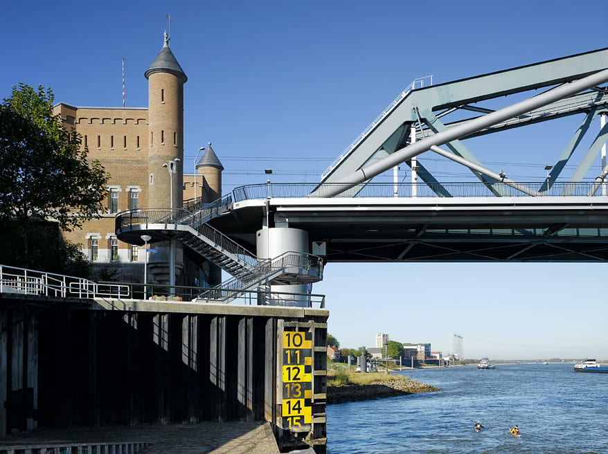 Het bakstenen landhoofd van de spoorbrug, met op de voorgrond een stalen trappentoren en een waterstandsmeter