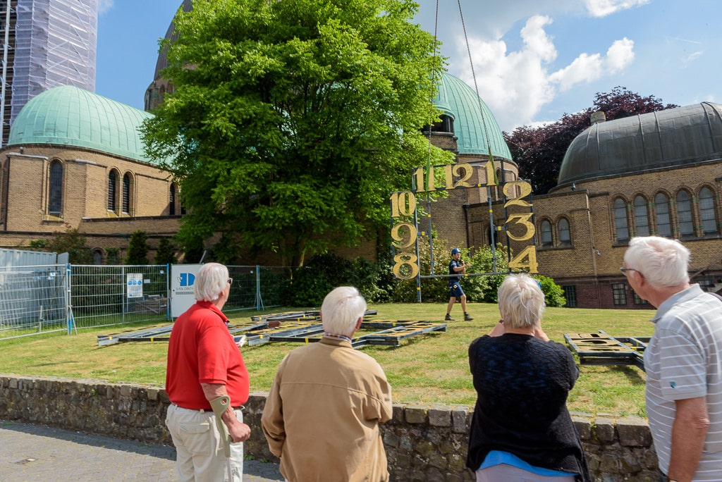 Voorbijgangers bekijken hoe de cijfers van de klok van de Sint Janskerk omhoog getakeld worden