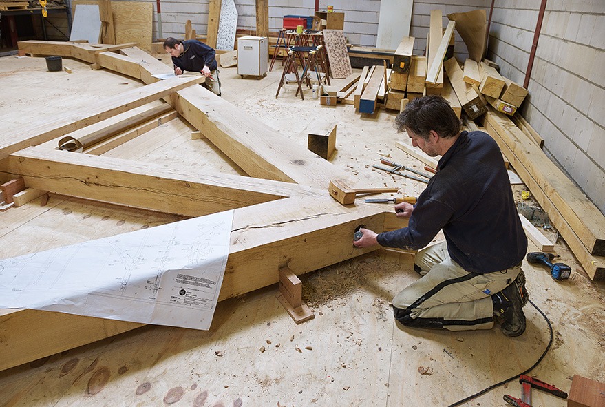 Medewerker van Van Dinther aan het werk aan een houten constructie in de timmerwerkplaats