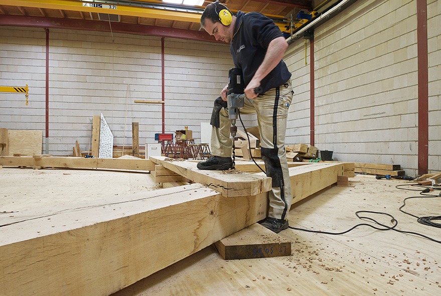 Medewerker van Van Dinther aan het werk aan een houten constructie in de timmerwerkplaats