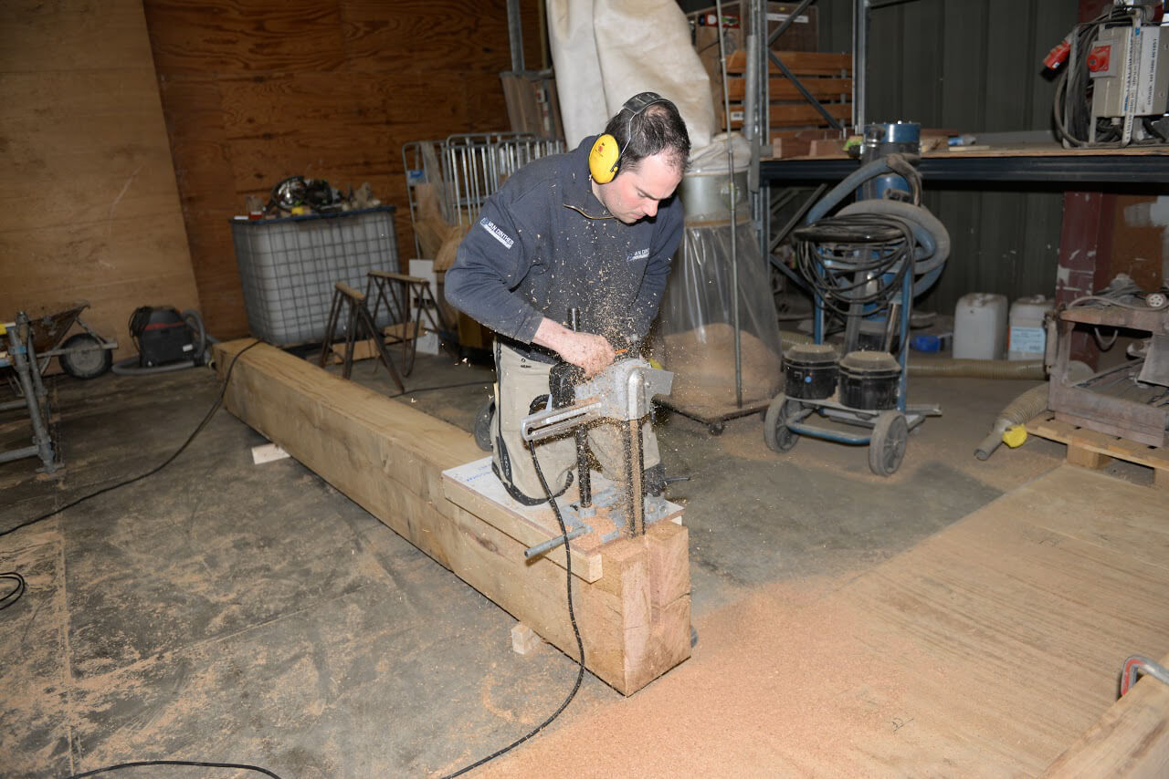 Medewerker van Van Dinther aan het werk aan een houten constructie in de timmerwerkplaats